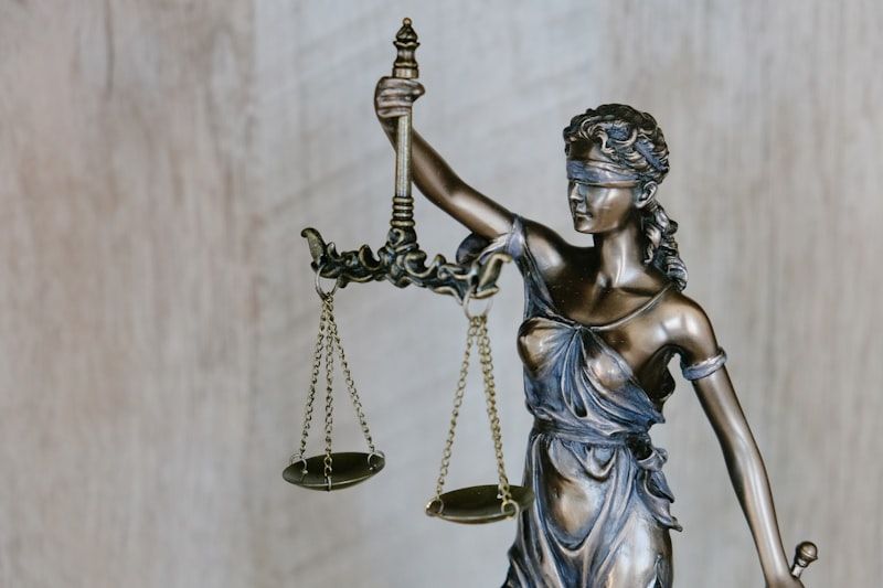 Een zilverkleurig beeld van een geblinddoekte Vrouwe Justitia met een grote weegschaal in haar rechter hand